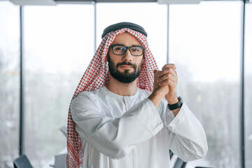 Young investor is standing. Successful Muslim businessman in traditional outfit in his office