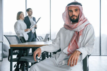 Serious facial expression. Muslim businessman in traditional outfit with colleagues in office