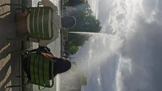 Multi-ethnic People Sitting in Front of Fountain at the Jardin des Tuileries. a couple of lovers sits in front of a fountain in Paris, Man and a woman look at the fountain, Slow motion. Vertical view