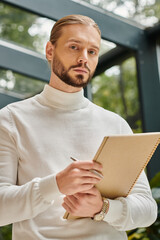 focused handsome architect in white comfy turtleneck with beard holding his paperwork on startup