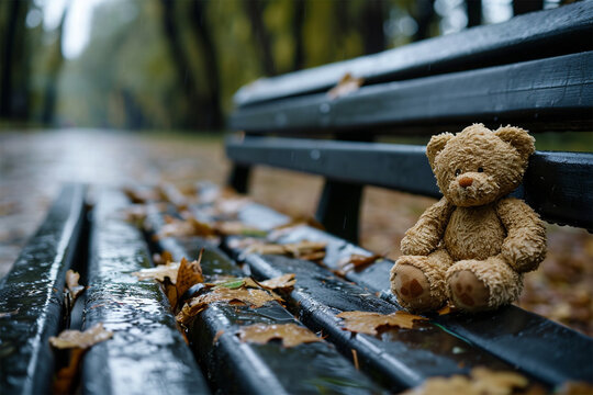 Lonely lost bear on a bench in a rainy park. Loneliness concept, International Missing Children's Day