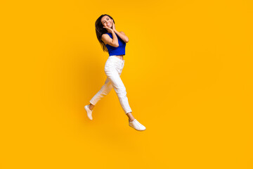 Fototapeta na wymiar Full length photo of dreamy adorable lady dressed blue top hands arms cheeks cheekbones jumping empty space isolated yellow color background