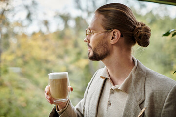 handsome appealing man with beard and collected hair in elegant suit drinking his hot coffee