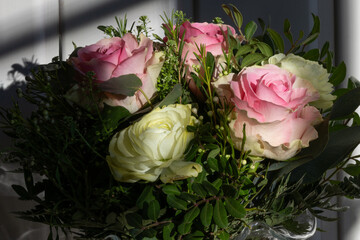 Nahaufnahme von einem Pastell Blumenstrauß von weißen und rosa Rosen angeleuchtet von der Winter Sonne draussen mit dem Schatten der Sprossenfenster