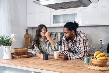 Young couple drinking coffee together in the kitchen on early morning before they go to the work. Emotional people spending free time with tea and conversation.