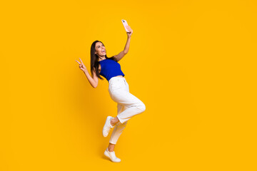 Fototapeta na wymiar Full length photo of funky impressed lady dressed blue top recording vlog modern device v-sign empty space isolated yellow color background