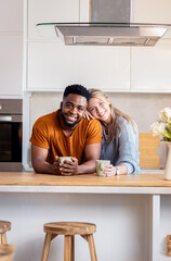 Portrait of smiling young mixed couple drinking coffee in kitchen at home.