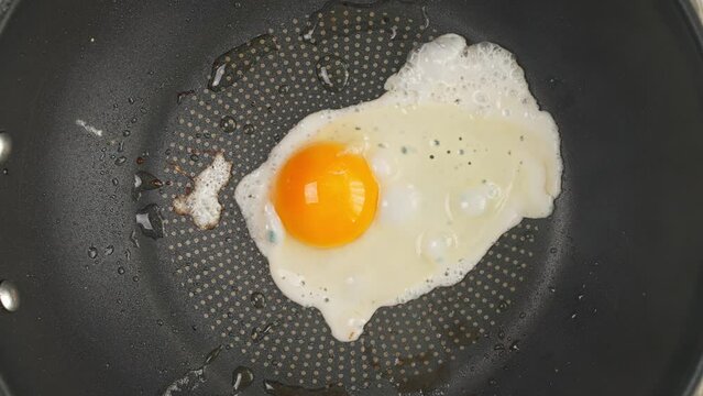 One egg fried in a frying pan top view. High quality 4k footage, Timelapse video of cooking a fried egg in a frying pan top view