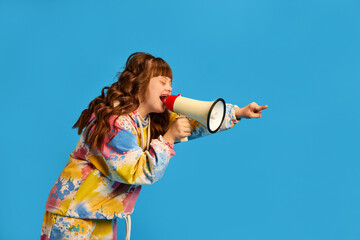 Health care awareness. Teen girl with down syndrome shouting in megaphone against blue studio background. Concept of acceptance, care, inclusion, health, diversity, emotions, social programs © master1305