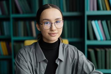 Focused young woman with glasses sitting in a library, intellectual poise.