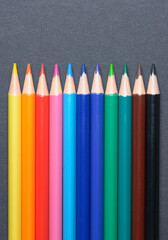 Collection set of colored pencils crayons orderly aligned in a row, art or drawing equipment on dark background.