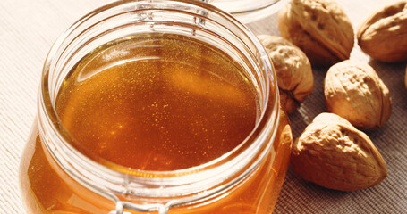 Organic liquid honey in a glass jar next to whole walnuts - 707864629