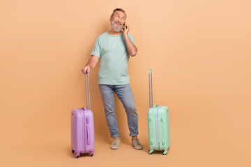 Full body photo of handsome man speak telephone hold suitcase look empty space isolated on beige color background