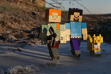 Obraz premium LEGO Minecraft figures of Alex with iron pickaxe, smiling Steve and pet friend Ocelot walking on frozen water surface in winter morning sunshine.