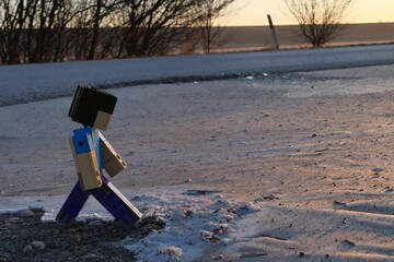 Fototapeta premium LEGO Minecraft figure Steve walking on ice frosty surface near asphalt road, sunlit by early morning winter sunshine.