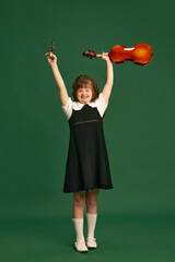 Beautiful girl with down syndrome standing with violin, learning music against green studio...