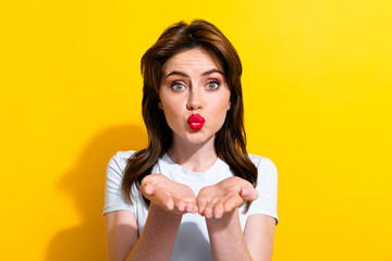 Portrait of good mood pretty girl with brunette hair wear white t-shirt sending air kiss to you isolated on yellow color background - obrazy, fototapety, plakaty