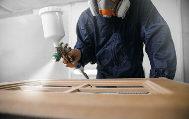 Professional worker staining wood furniture with spray gun - obrazy, fototapety, plakaty