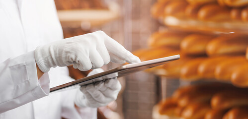 Baker woman in chef uniform use tablet computer for control quality of craft bread in bakery...