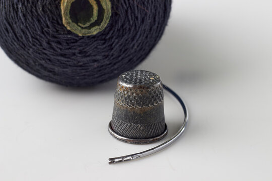 Metal thimble, sewing needle and spool of black thread on a white background