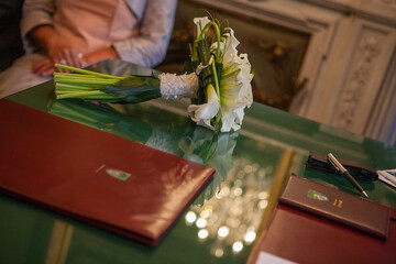 Naklejka na ściany i meble This photograph captures the poetic stillness of a bridal bouquet resting on the signing registry, a moment frozen in the midst of matrimonial proceedings. The bouquet, composed of white lilies and