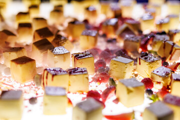 The set of bite-sized small cheesecakes on a white surface. Berries, sugar powder, and chocolate are used as decor.