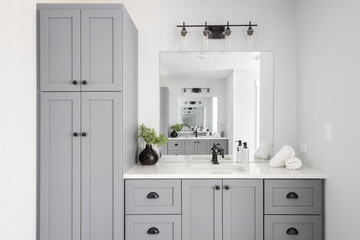 A renovated modern farmhouse bathroom detail with grey cabinets, decorations on a white marble countertop, and rubbed bronze faucet.