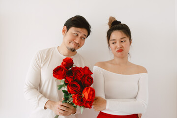 Asian man giving red rosed and flirting proposal, woman sulk and dislike flowers and ignoring reject, both standing isolated over white background wall. 