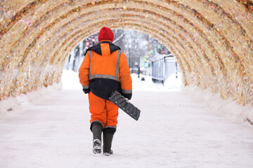 Worker with shovel walking on festive decorations backgrond, snow removal in winter city