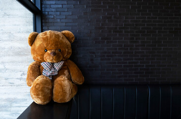 Teddy bear is sitting on black sofa