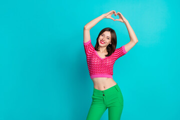 Portrait of pleasant optimistic girl with stylish hair wear pink top showing heart symbol over head isolated on blue color background