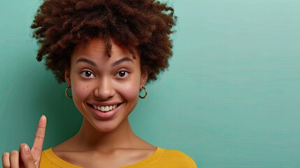 Cheerful afro black young woman, pointing with the finger, isolated on plain green background.