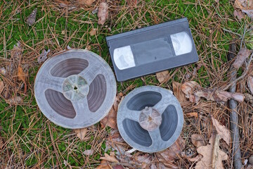 a set of two old magnetic reels and a video cassette lie on the ground and green moss on the street