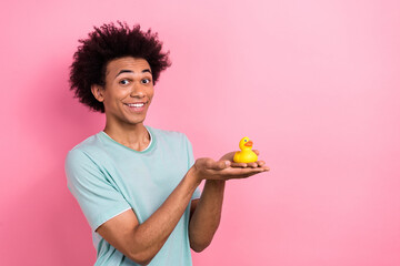 Photo of cheerful funky guy wear blue t-shirt holding arm rubber duck empty space isolated pink...
