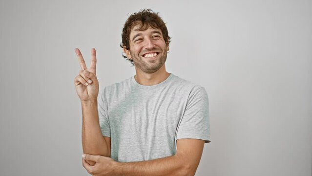 Cheerful young man winks and flashes two-finger victory sign, radiating the winning spirit. happy, winking face. donning a nice, casual t-shirt. isoleted against a spotless white background.