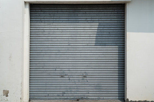 Closed metal grate rolling door of the warehouse storage or service garage. View from in front of the building, industrial building place.