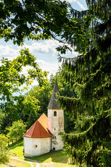 Landscape of Slovenia. A small white church is nestled in the mountain between meadow and forest - 707951217
