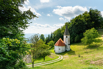 Landscape of Slovenia. A small white church is nestled in the mountain between meadow and forest - 707951274