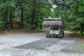 Bobcat mini loader is moving bucket of crushed stone gravel during construction operations