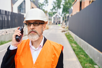 Serious foreman using hand-held radio transceiver on development site