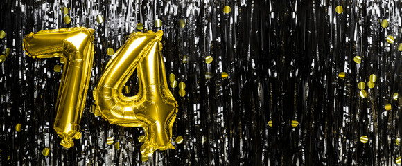 Gold foil balloon number number 74 on a background of black tinsel decoration. Birthday greeting...
