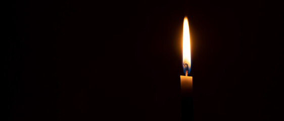 A single burning candle flame or light is glowing on a small orange candle on black or dark...