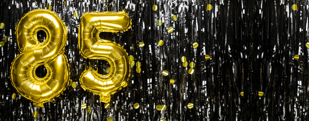 Gold foil balloon number number 85 on a background of black tinsel decoration. Birthday greeting...