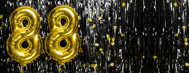 Gold foil balloon number number 88 on a background of black tinsel decoration. Birthday greeting...