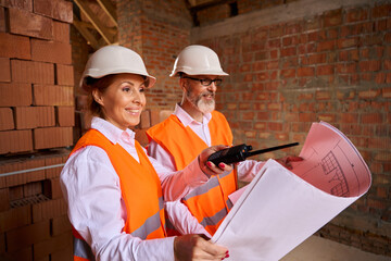 Building inspector and contractor are using blueprints during site inspection