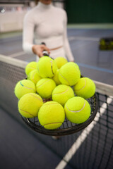 Unknown woman player in white attire holding lots tennis balls on racket