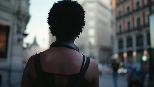 Young African American woman exploring amidst golden hour glow of bustling metropolis during touristic trip. Black female walk at evening street enjoying summer travel to Madrid