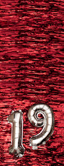 Silver foil balloon number number 19 on a background of red tinsel decoration. Birthday greeting...