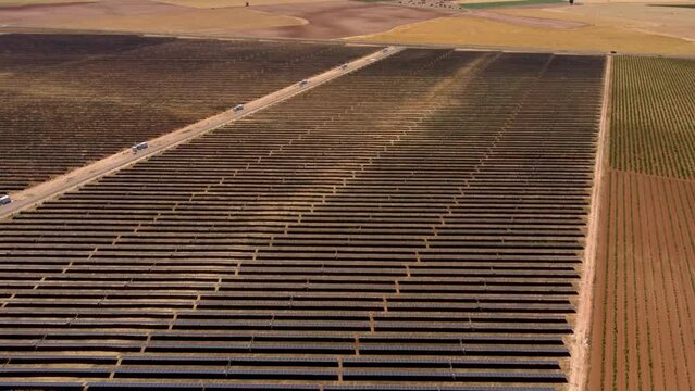 Aerial view of solar plant farm surrounded by farmland with different crops. Renewable ecological source of energy from the sun. Brone backwards and camera tilt up revealing all the landscape.