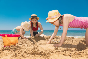 Children in sun hats building a sandcastle on a beach